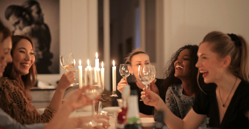 Women laughing over candlelight at a long dinner table